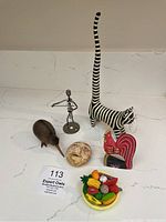 Overview image of all six oddities: striped cat figurine, metal man, brown bird, rooster head, miniature fruit bowl, and face sculpture.
