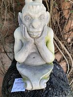 Front view of cast stone gargoyle sculpture showing facial features and hands supporting the head.
