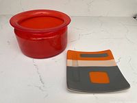 Two-piece lot: translucent orange glass bowl with wide rim on left, geometric fused glass square plate on right