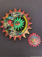 Two handpainted sun and moon wall hangings, larger signed TAXCO, showing vibrant colors and folk art style.