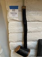 Full view of the black painted wooden shillelagh club leaning against a wall, showing the overall length and shape.