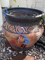 Side view of large southwestern style terra cotta planter with two handles, hand painted with colorful motifs including blue, red, white, and black. Wide black rim and rounded shape.