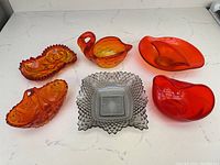 Top view of six midcentury glass pieces including five orange glass and one smoked gray glass piece arranged on a white surface