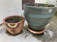 Photo showing both the green ceramic pot (right) and the terracotta pot with floral design (left) placed outside on concrete.