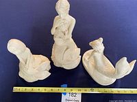 Top-down view of the three L Wilson mermaid sculptures arranged next to a measuring tape indicating about 10.5 inches in height