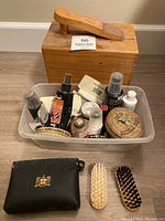 Plastic bin filled with various shoe polishes, sprays, and a small leather pouch holding two shoe brushes