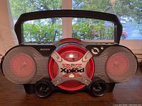 Front of Sony Xplod boombox showing large speakers, central red CD compartment with Xplod logo, black casing and handle.