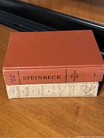 Stack of two hardcover books by John Steinbeck, showing the cover and spine of both books on a wooden surface