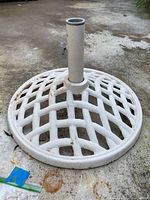 Full view of white wrought iron umbrella stand with lattice base on concrete surface