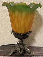 Frontal view of the lamp showing the green and amber glass shade and sculpted brass base with drummer figurine.