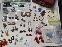 Full overview of vintage and contemporary jewelry collection with various earrings, brooches, bracelet, and shoe figurines, including items in clear ziplock bags