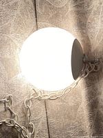 Photo of the lit white round globe lamp with metal top and attached chain, showing working illumination and lamp details.