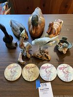 View of all wooden bird decoys and figurines arranged on a table along with four round pelican tile coasters.