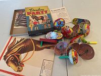 Overview of the Pin the Tail on the Donkey game box, poster, paper tails, instructions, and several metal noisemakers with vibrant colors.