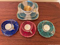 Top view of five Bavaria tea cups each paired with a saucer and matching dressers plate for one set. The sets are arranged on a wooden surface, showing detailed color and gold accents.