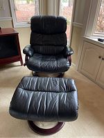 Black vinyl swivel recliner chair with padded armrests and headrest, showing wooden accents and the cushioned seat with some creases from use.