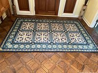 Full view of the rectangular blue patterned hooked rug on wooden floor in entrance area.