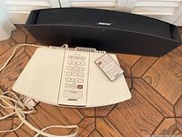Photo showing Bose Wave Radio/CD main control unit, black speaker, and remote on tiled floor.