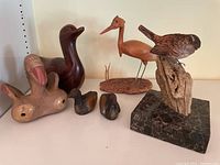 Group of six bird carvings displayed on a shelf, showing various materials and sizes including wood and ceramic items.