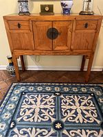 Full front view of the wooden console cabinet with visible drawers, doors, and legs standing on a patterned rug.