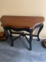 Wooden console table with distinctive black curved legs and warm brown curved top, showing overall design.