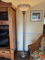 Full view of the floor lamp next to wooden furniture and a wicker chair showing overall height and metal base design.