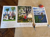 Three colorful posters laid out on floor with tape measure and utility knife, showing full artwork and edges.