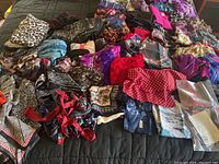 Top-down view of large scarf assortment laid on a bed showing various colors and patterns including animal prints, florals, stripes, and polka dots.