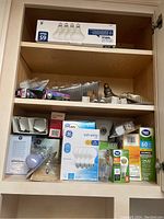 Large assortment of light bulbs and bulb boxes inside a wooden cabinet shelf.