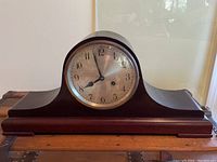 View of the full German mantle clock with wooden case in tambour style and round clock face centered.