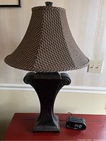 Full view of one lamp showing brown metal base with carved details and brown patterned fabric shade with bell shape.