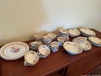 Pareek Johnson Bros England bone china dinnerware set displayed on wooden surface featuring plates, cups, saucers, and bowls with floral and gold accents.