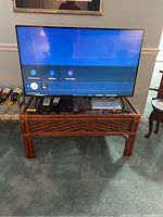 Samsung 44 inch flat screen TV powered on showing user interface on screen, on wooden stand with remote and cables.