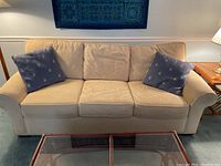 Front view of the vanilla-colored Sealey sleep sofa with three seat cushions and two blue polka dot throw pillows on each end, placed in a living room setting.