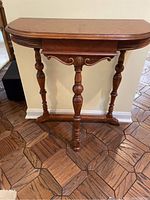 Front view of small wooden console table showing decorative turned legs and carved apron on a parquet floor.