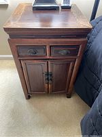 Front view of small wooden cabinet showing two drawers and two doors with metal latch and pulls.