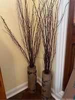 Two of the three antique wallpaper rolls positioned side by side on a herringbone wood floor corner with pussywillow branches inside.