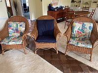 Front view of three wicker rattan armchairs arranged in a living room with cushions. Two feature printed cushions and one has solid blue cushions.