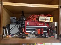 Wide view showing the Craftsman red toolbox, Black & Decker cordless drill, orange extension cord, jumper cables, assorted small tools and hardware items.