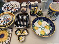 Wide shot showing assortment of Tuscan and Polish pottery including plates, bowls, trays, cups, oil and vinegar set, and utensil holder with various floral and fruit designs.