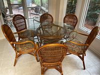 Full view of round glass top table surrounded by six rattan chairs