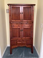 Front view of tall wooden cabinet with bamboo vertical slatted doors and drawers, showing the entire piece standing on carpet.