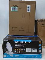 Photo showing packaging of 2 boxed Oulton floor lamps with remote control outline and a boxed 12 pack of Ensenior 6-inch recessed LED ceiling lights with color temperature options. One box shows slight wear.
