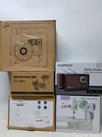 Five original boxes stacked displaying the items: Vintage style turntable, solar sensor light, low voltage transformer, Looptone Retro Radio, Magicfly Mini Sewing Machine.