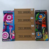 Photo of the full lot showing 2 colorful archery toys in original packaging on both sides with 4 brown cardboard boxes labeled 'TOY MODEL' in the center stacked vertically.