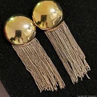 Pair of earrings with gold tone domed tops and multiple fine sterling silver chain strands hanging as fringe, shown on black background.