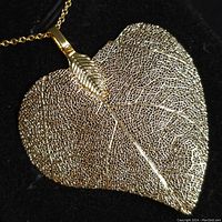 Close-up front view of gold-colored heart-shaped leaf pendant with detailed vein structure attached to a chain.