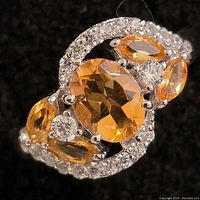 Close-up photo showing the oval faceted citrine center stone, marquise-shaped citrines, and surrounding cubic zirconia on a silver band.