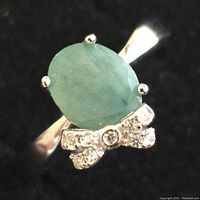 Close-up front-top angle of the silver ring featuring the oval emerald and bow accent