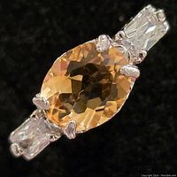 Close-up view of the oval faceted citrine center stone flanked by rectangular clear CZ stones set in silver prong setting.